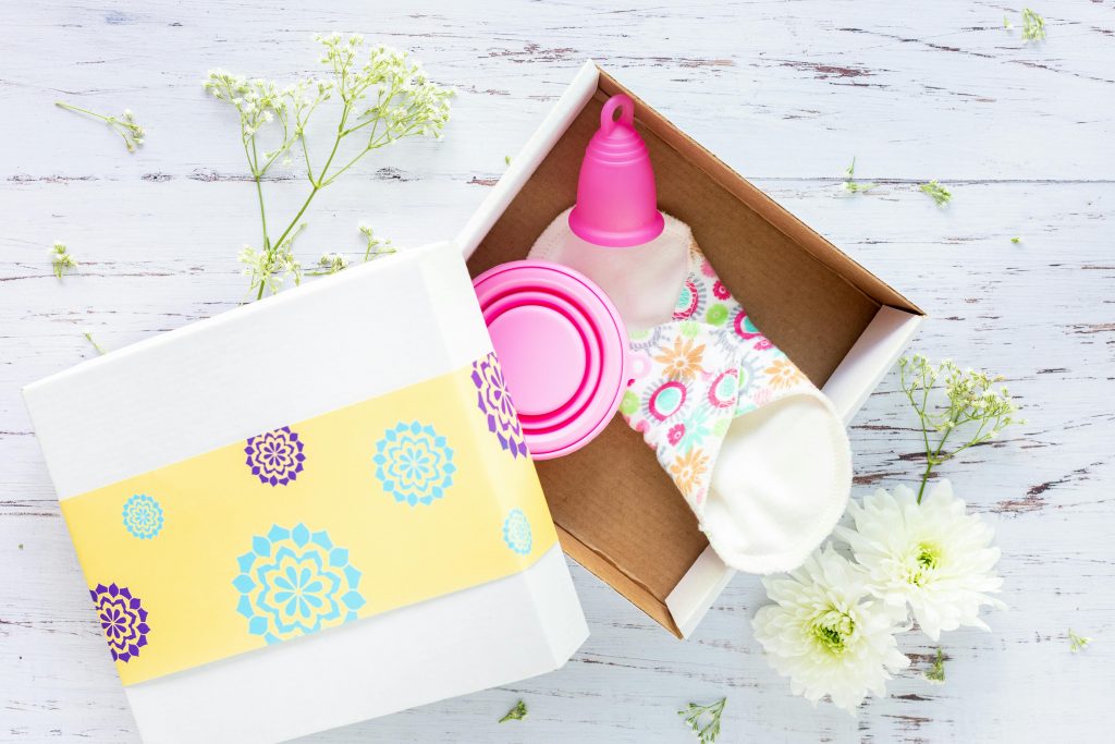 pexels-photo-1560288-1560288 Brightly decorated gift box containing reusable menstrual cup and pads on a rustic background.