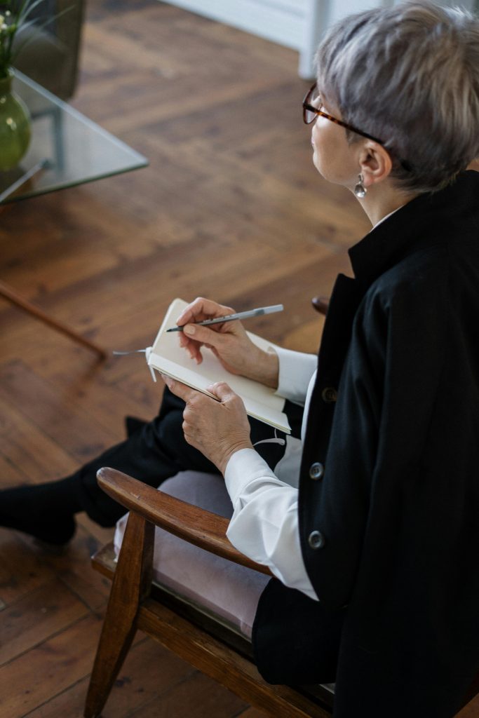 pexels-photo-4098148-4098148 A professional woman with glasses taking notes while seated indoors, depicting consultation or therapy.