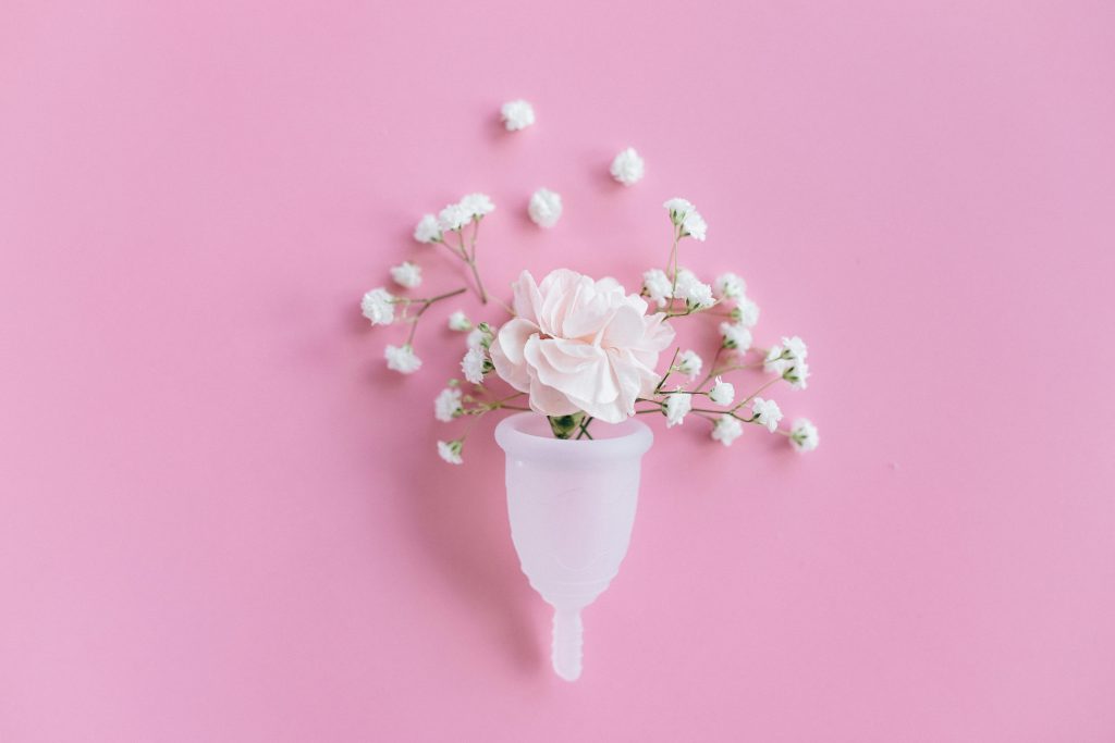 pexels-photo-5712300-5712300 A menstrual cup filled with delicate flowers on a pink background, symbolizing feminine care and eco-friendly solutions.