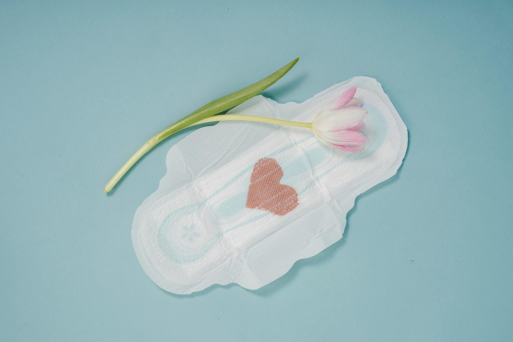 pexels-photo-5938447-5938447 A menstrual pad with a pink heart and tulip on a blue surface, symbolizing care and femininity.