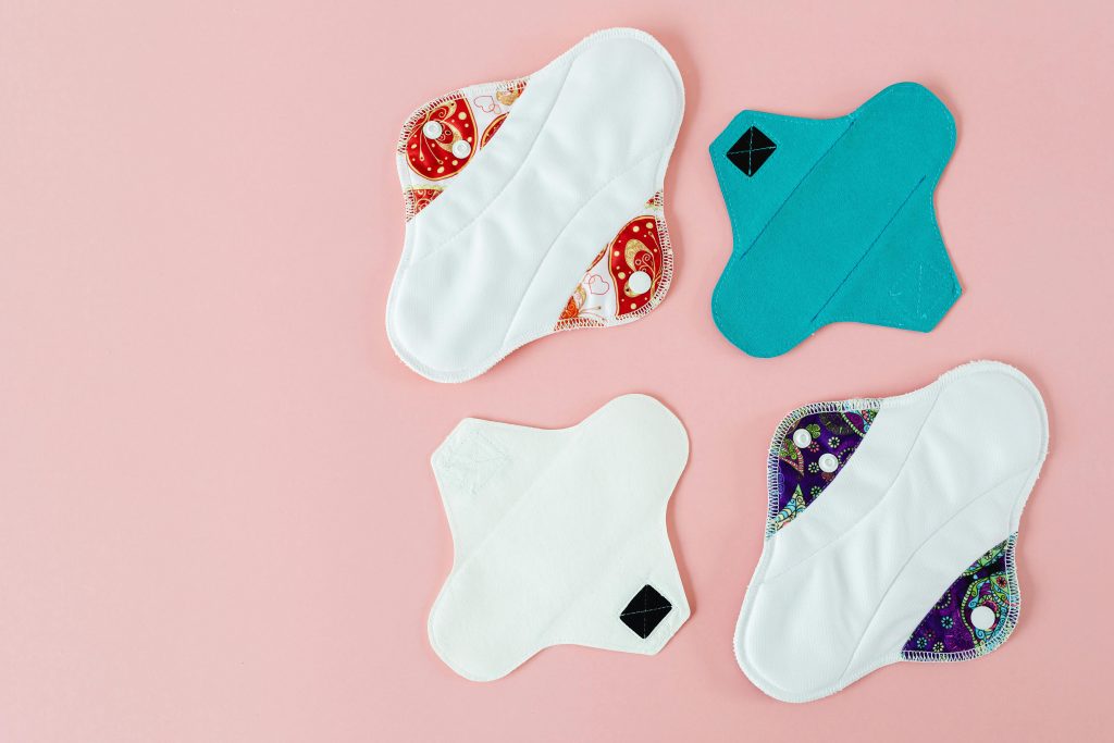 Collection of colorful reusable menstrual pads on a pink surface, showcasing environmentally friendly hygiene products.