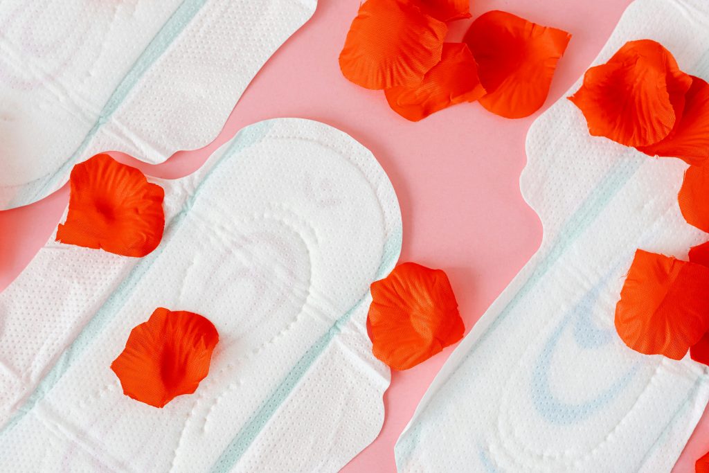 pexels-photo-7692266-7692266 Close-up of sanitary pads with red petals on a pink background, symbolizing menstruation.